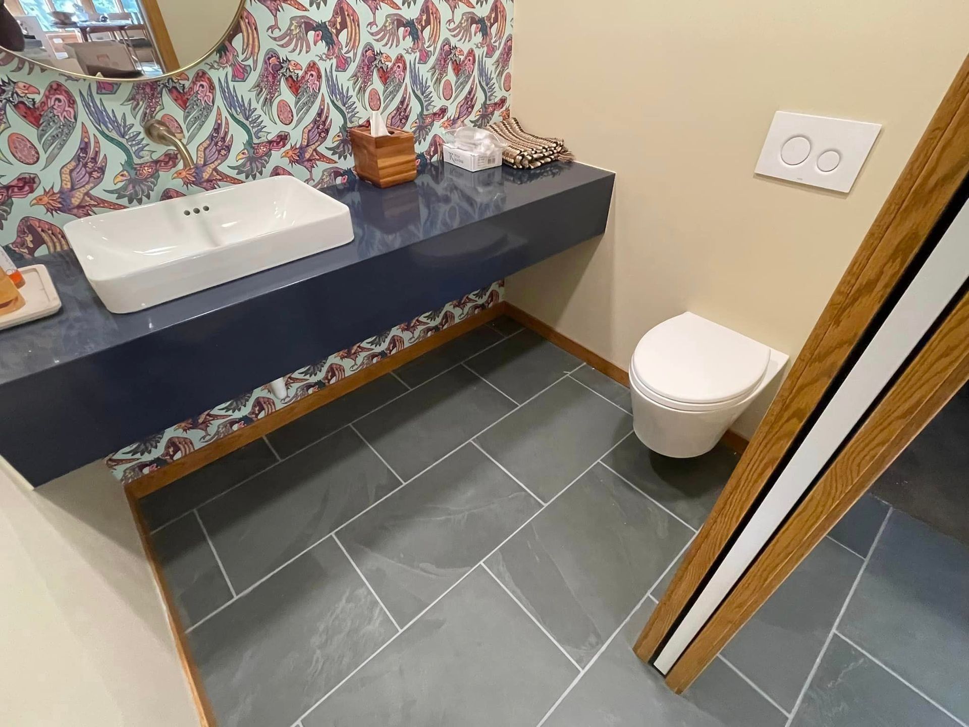 Modern bathroom with a floating sink, patterned wallpaper, and dark tile floor.