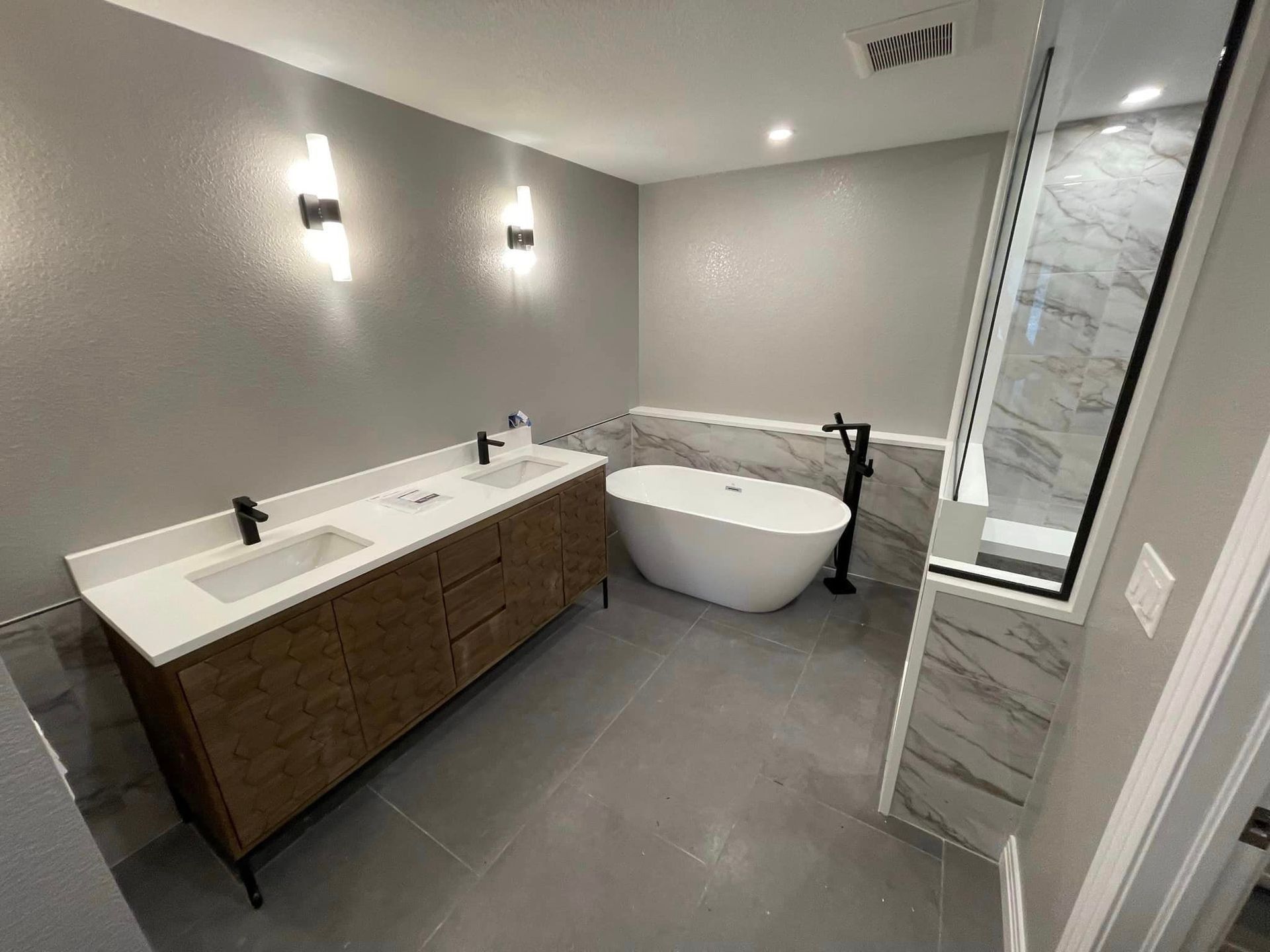 Modern bathroom: double vanity, freestanding tub, marble shower, gray walls, and sconces.