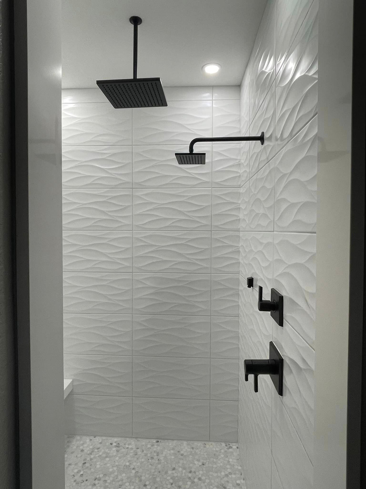 Modern white tiled shower with textured walls and black fixtures.