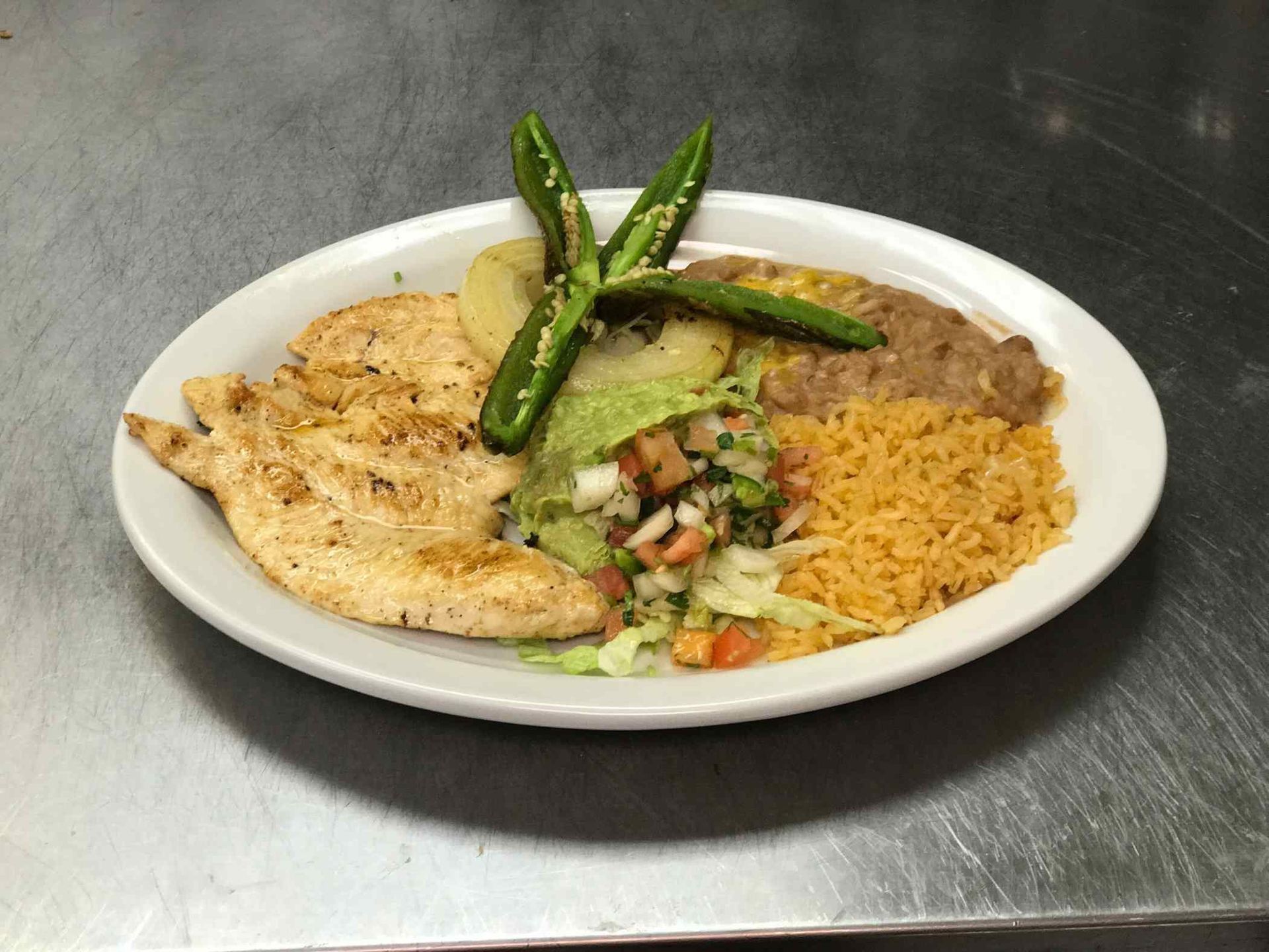 A white plate topped with chicken , rice and beans on a table.