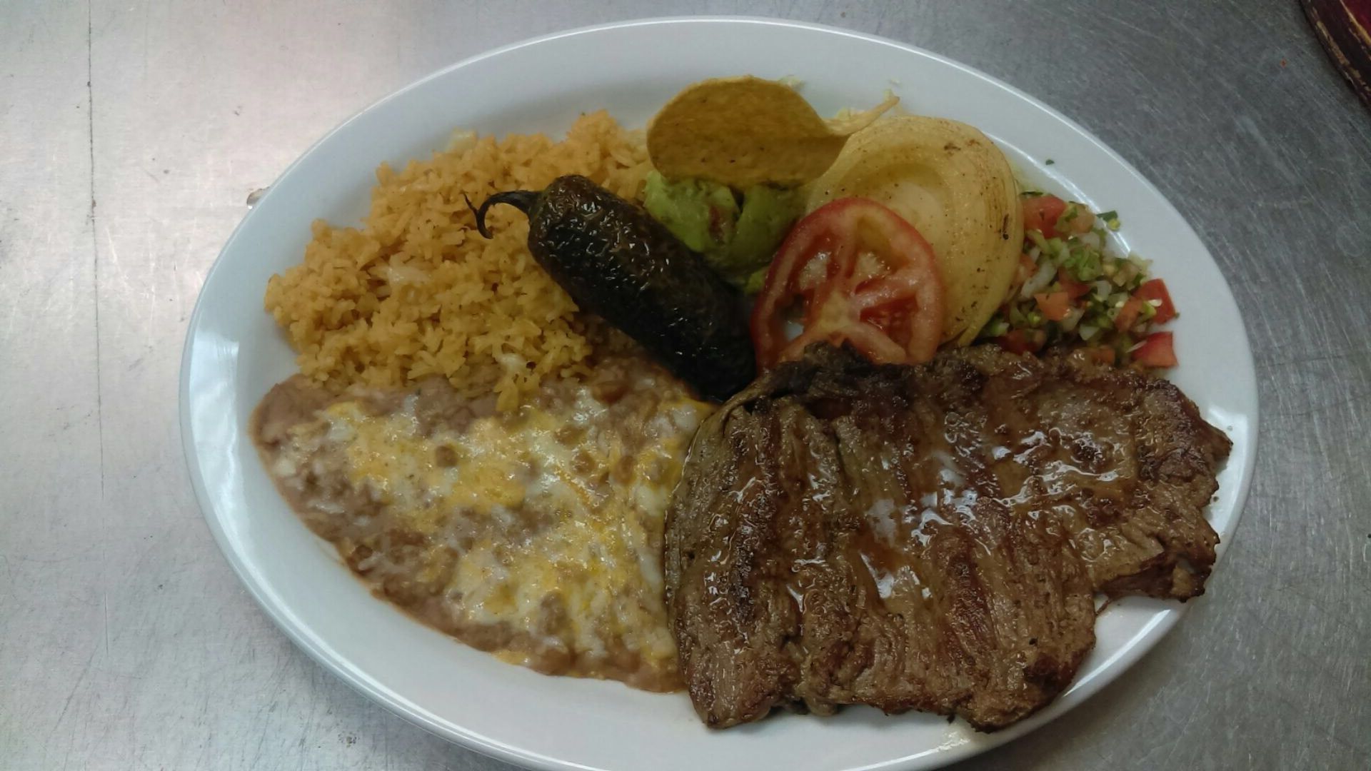 A white plate topped with a steak , rice , beans and vegetables.