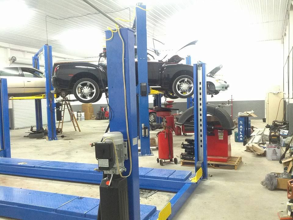 A mechanic shop with two cars on lifts. One black truck and a white car. Equipment and tools visible.