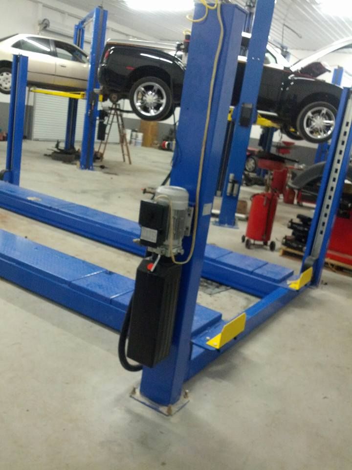 Blue car lift in a garage with two vehicles elevated.