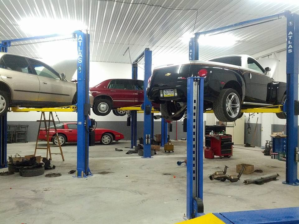 Cars on lifts in a brightly lit auto repair shop, showing maintenance work in progress.