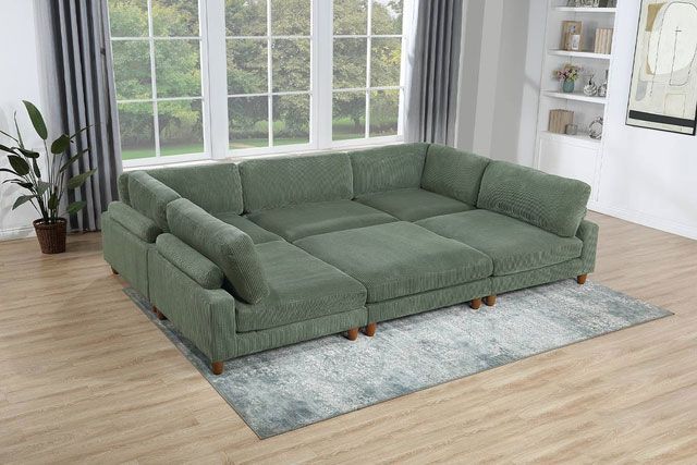 A large green sectional couch is sitting on top of a rug in a living room.