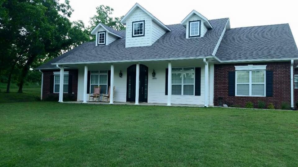 A white, two-story house with a dark gray roof, brick accents, and a porch on a green lawn.
