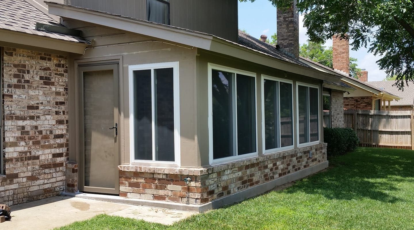 Sunroom with a brick base and multiple windows attached to a house with a brick exterior and a green lawn.