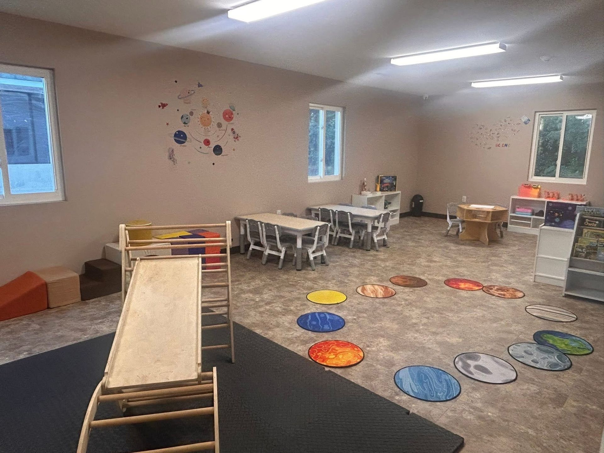 Playroom with tables, slide, planet-themed rugs, and artwork on a tan wall.