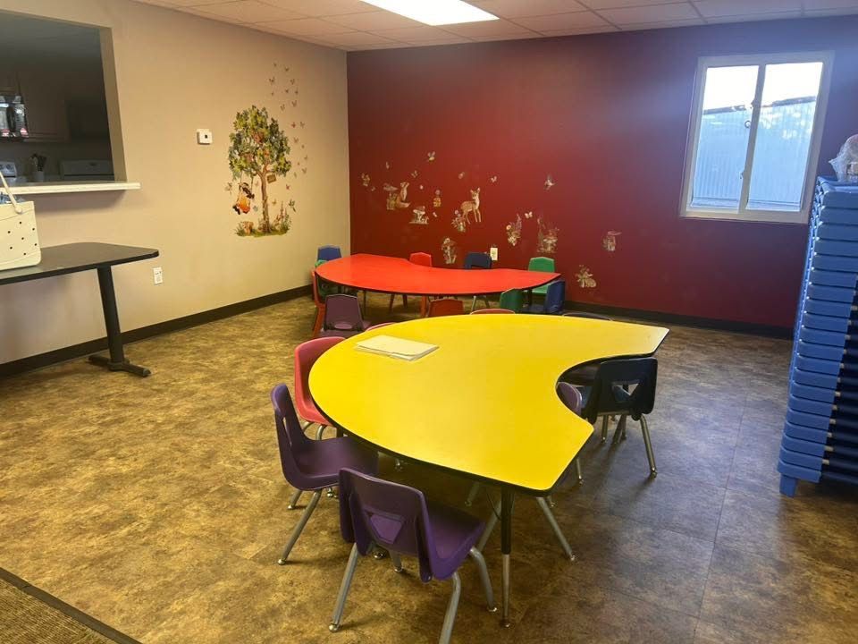 Classroom with colorful tables, chairs, and decorated walls; likely a daycare or play area.