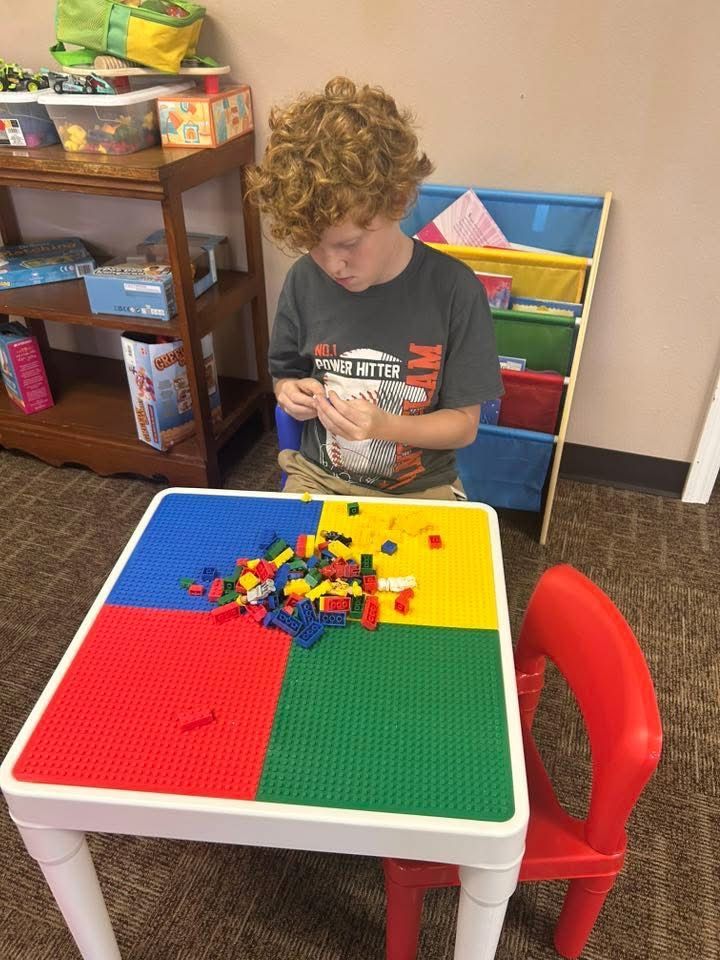 Boy with curly red hair builds with Legos on a colorful table, indoors.