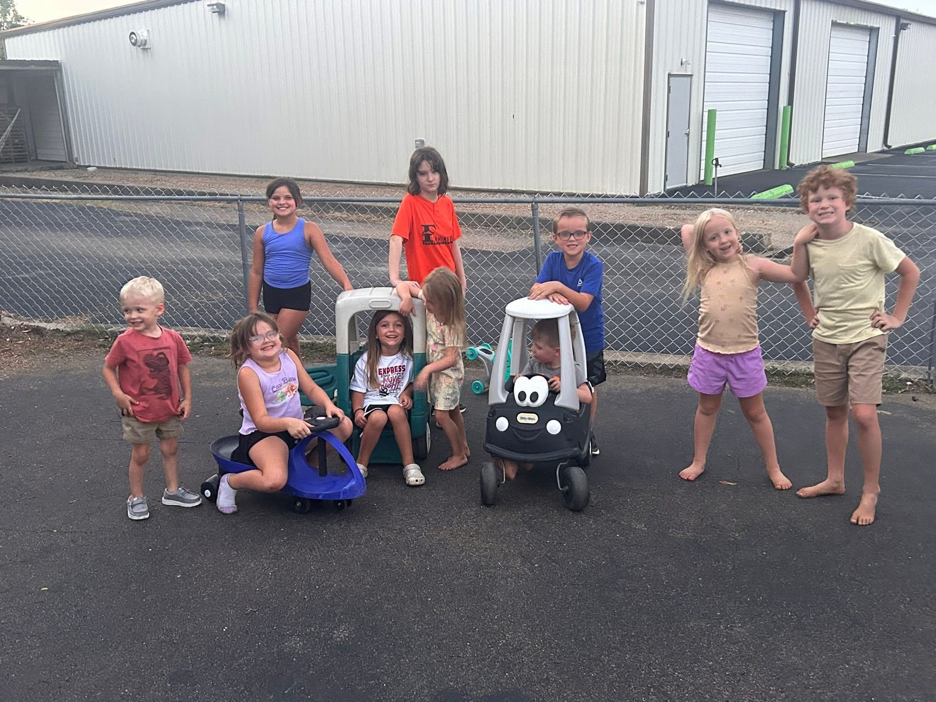 Group of children playing outside; some with toy cars, smiling.