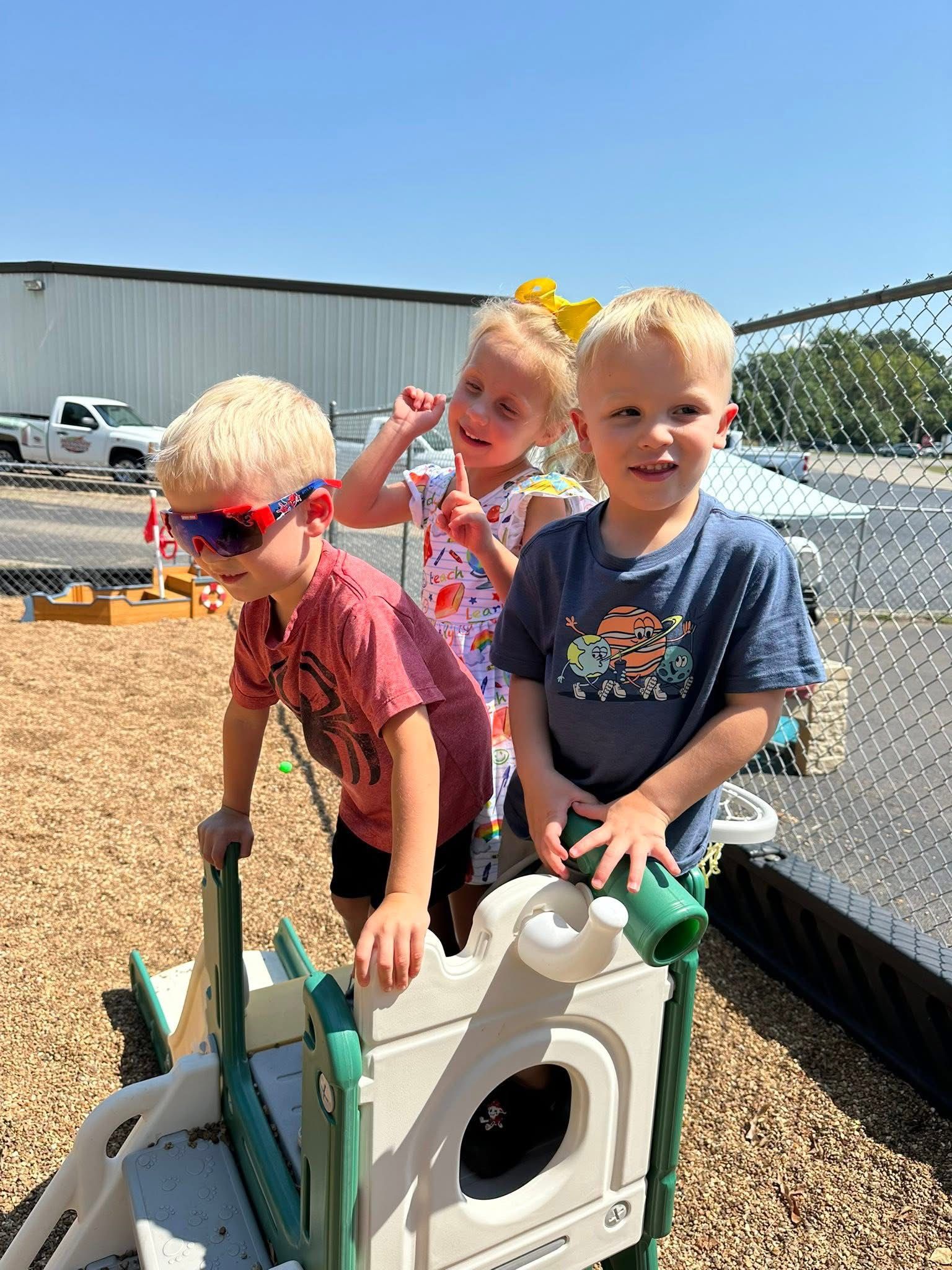 Three kids playing on a plastic playground slide on a sunny day.