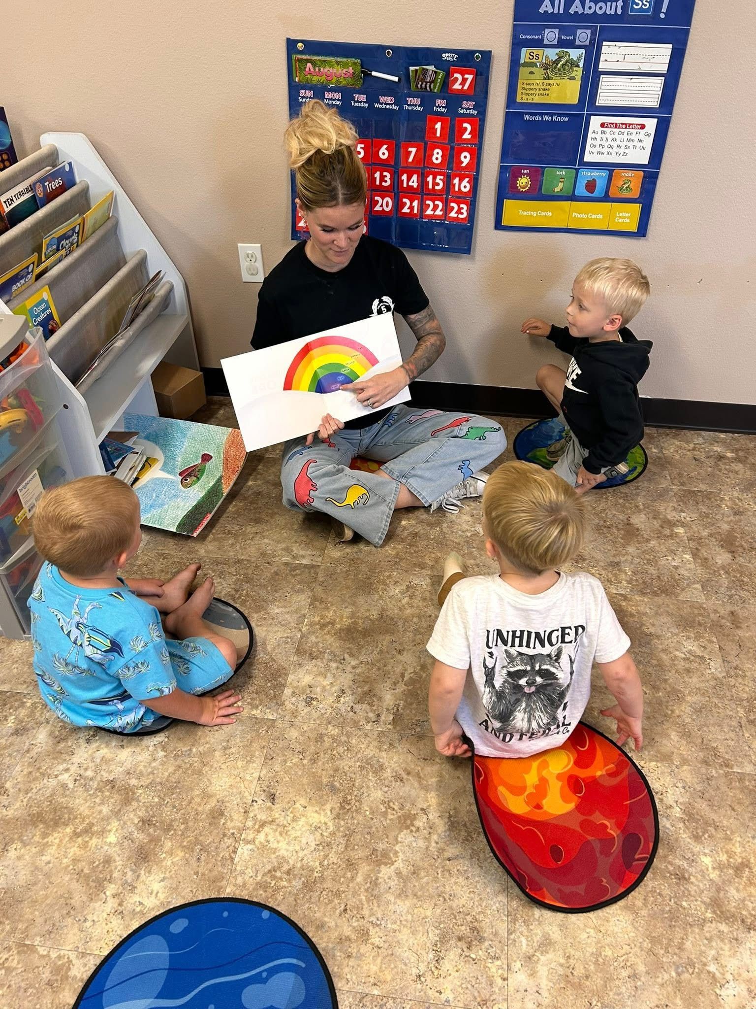 Teacher shows a rainbow drawing to three young children in a classroom.