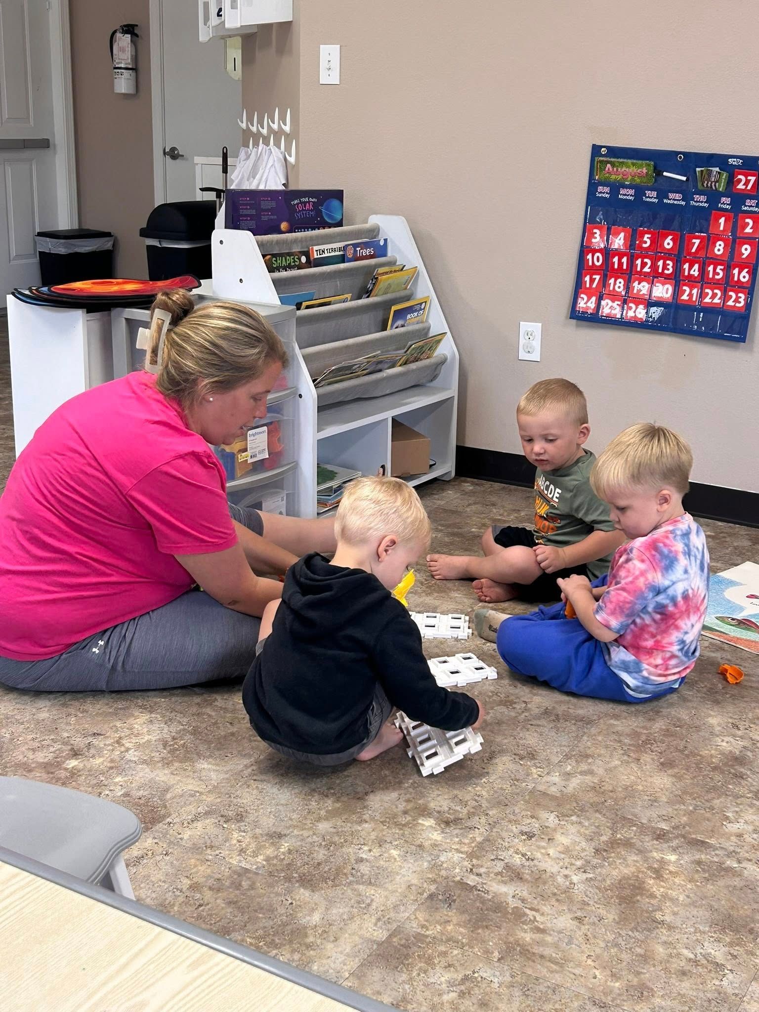 Teacher and three toddlers playing on floor in classroom.