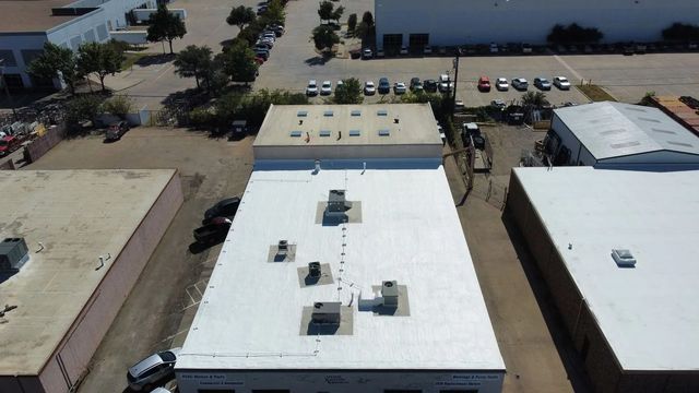 Aerial view of flat white rooftops in an industrial area with parked cars and buildings nearby