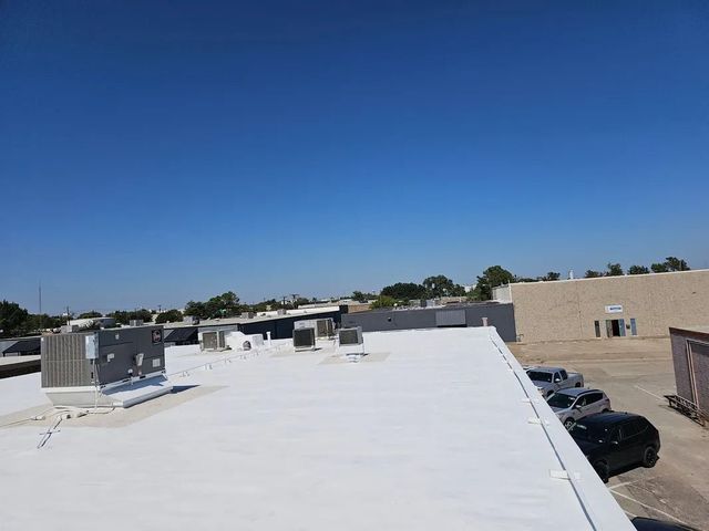 Rooftop with white surface, HVAC units, parked cars, and a clear blue sky