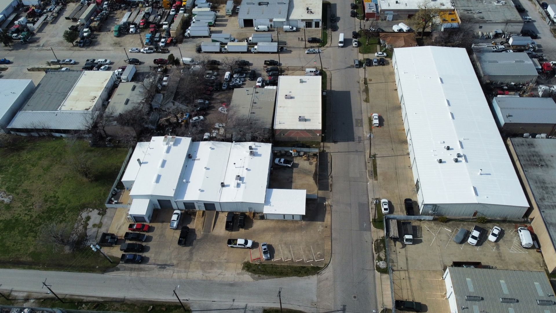 Aerial view of an industrial yard with white-roofed buildings, parked vehicles, and a central road.