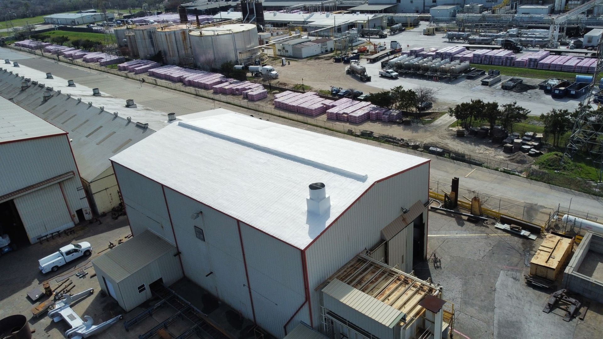 Aerial view of a large white warehouse beside rail lines and industrial buildings.
