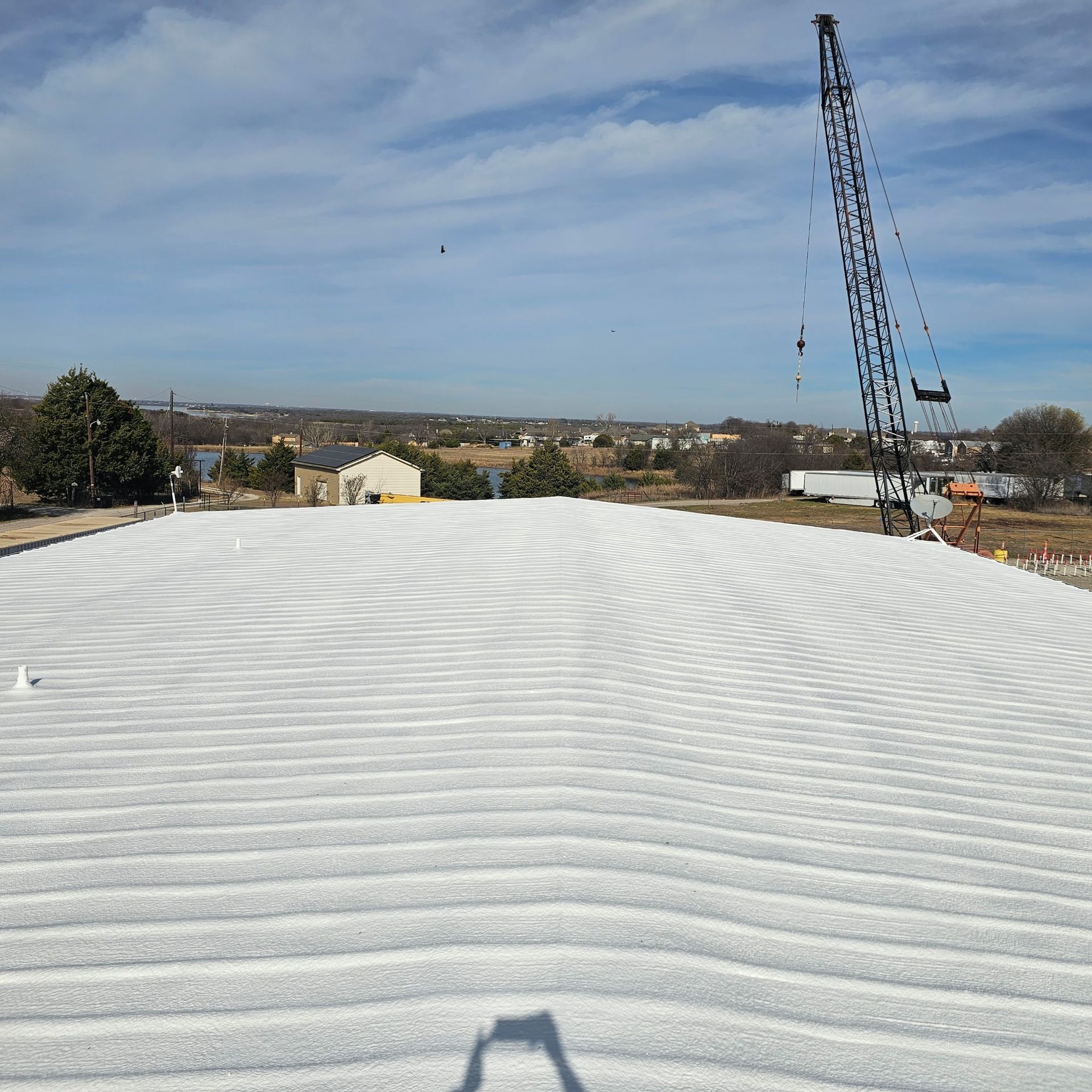 White corrugated roof in foreground with a crane and distant buildings under a blue sky