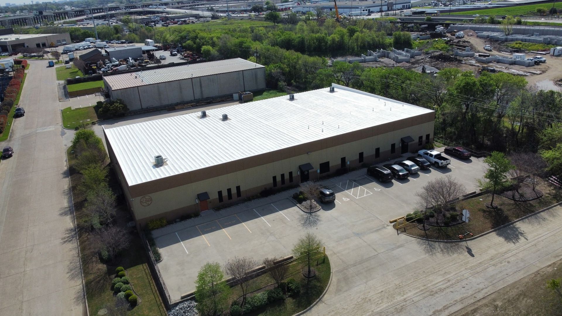 Aerial view of a beige warehouse with white roof and parked cars beside a road and lot