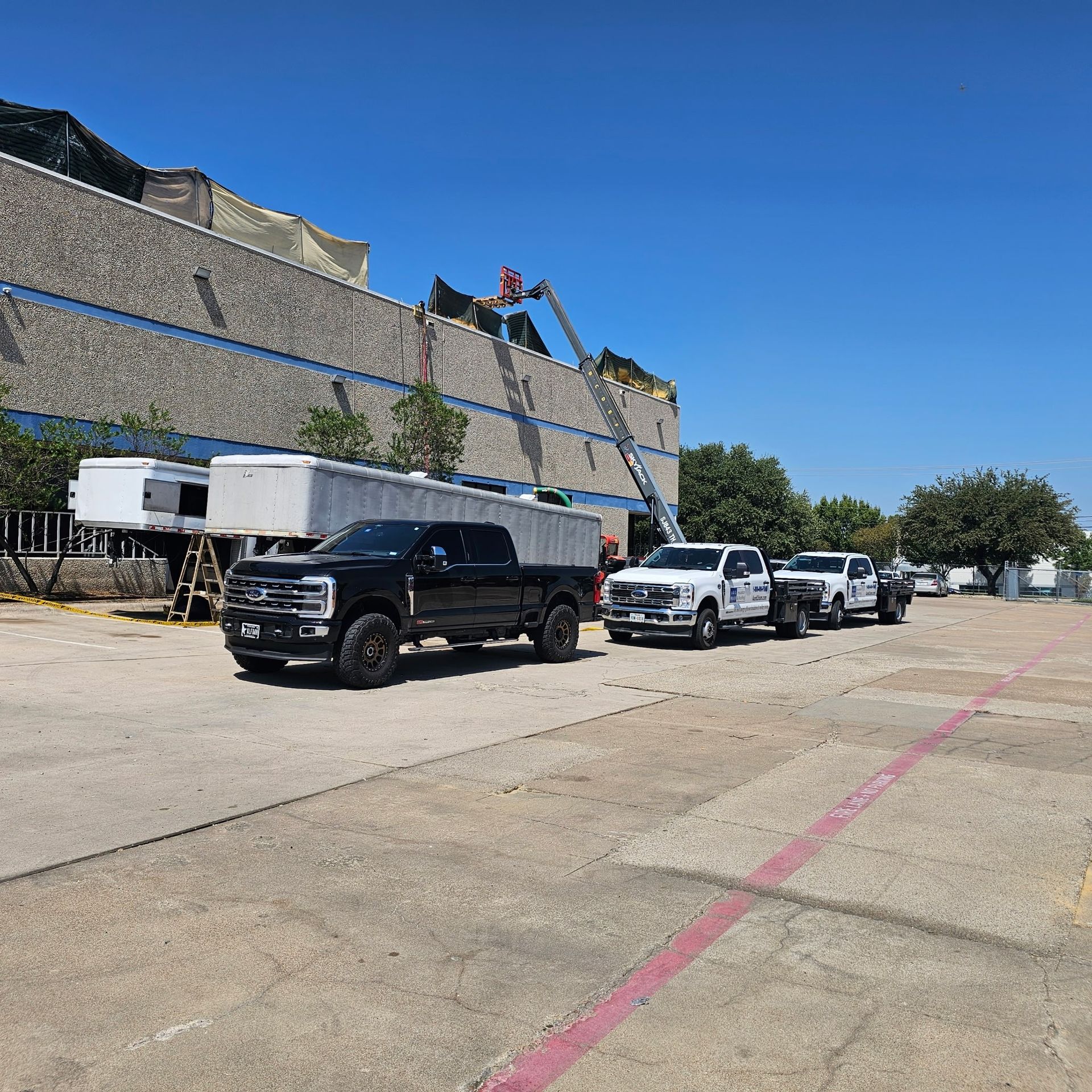 Black pickup and white work trucks parked beside a stone wall under a blue sky.