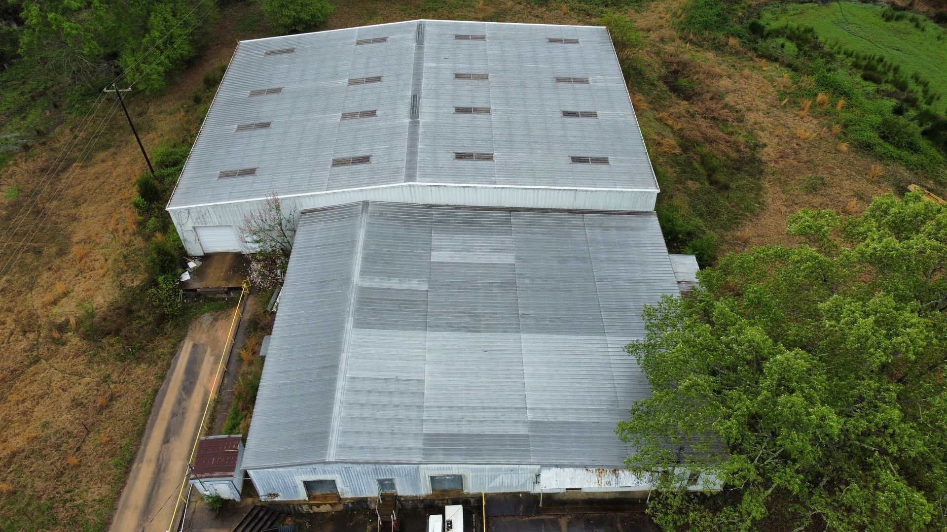 Aerial view of a large corrugated metal-roof building surrounded by dense green vegetation.