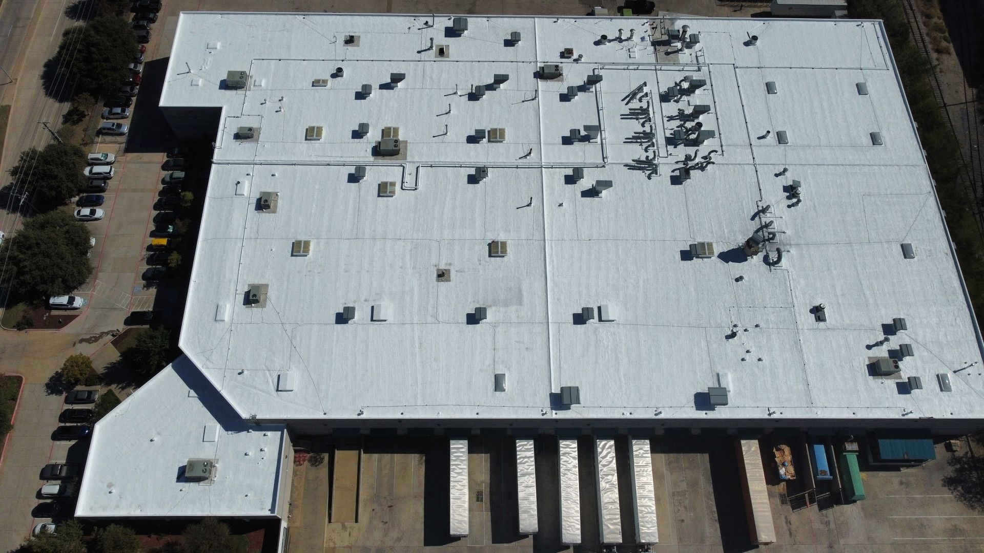 Aerial view of a large white-roofed warehouse with rooftop equipment and trucks at loading docks
