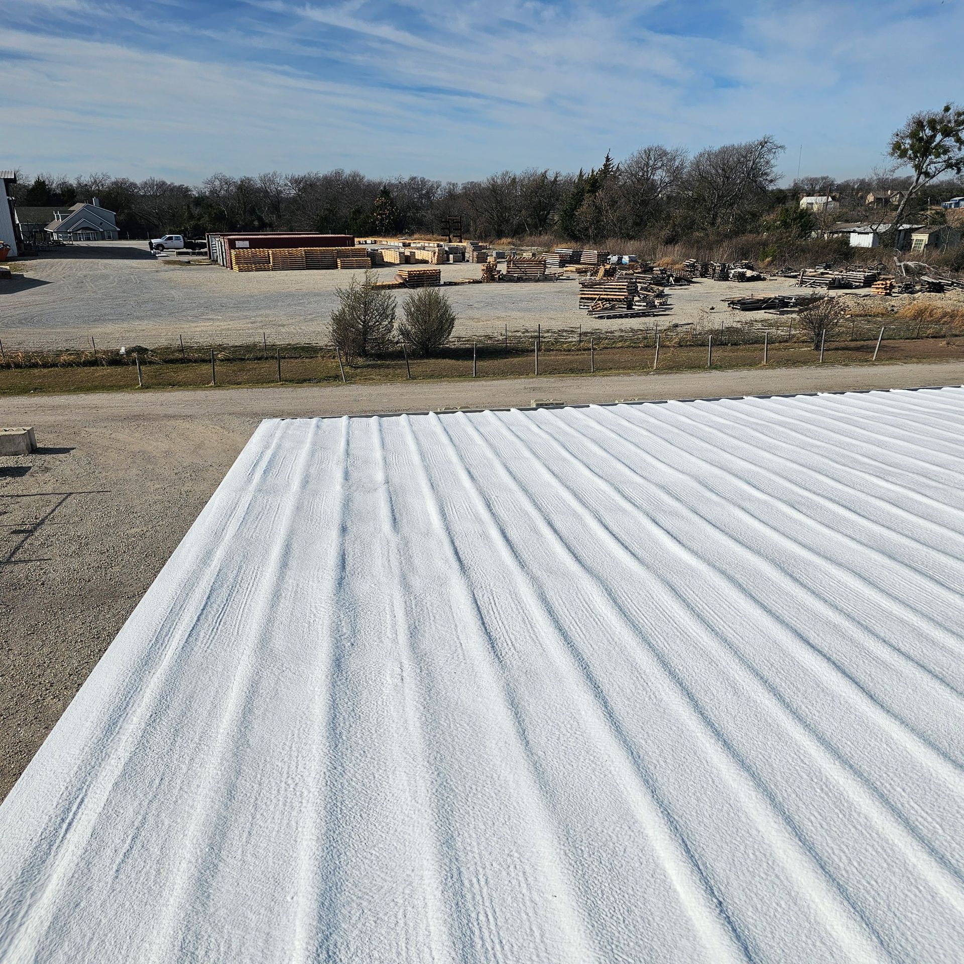 White corrugated roof panels in the foreground, with an open rocky lot and scattered equipment beyond.