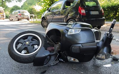 A motorcycle has crashed into a car on the side of the road.