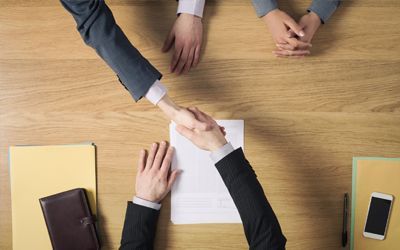 A man and a woman are shaking hands over a piece of paper.