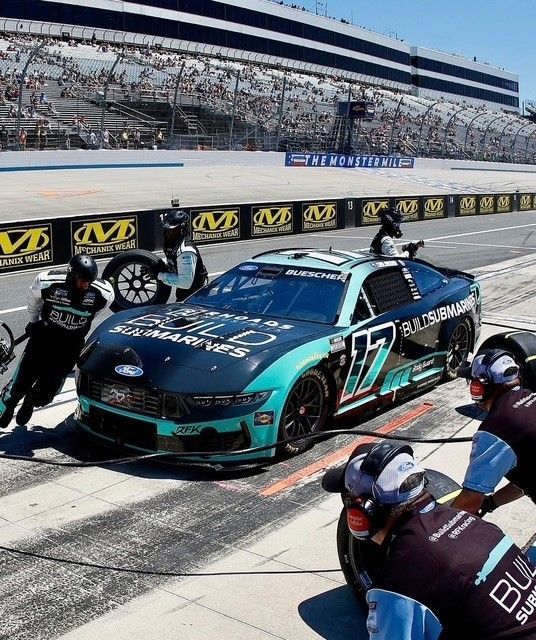 Teal NASCAR stock car in pit lane with crew members beside it at a racetrack
