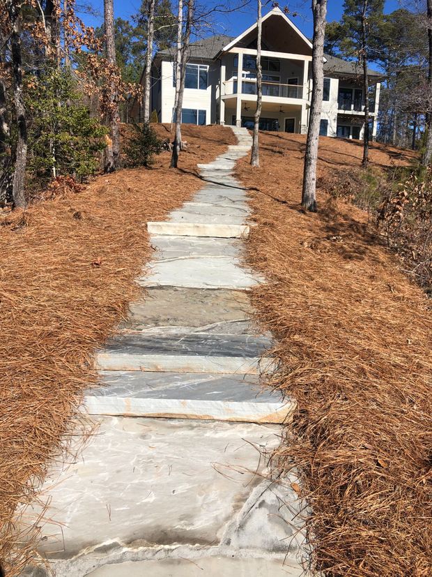 Stone steps leading uphill to a multi-story house on a hillside, surrounded by fallen leaves and trees.