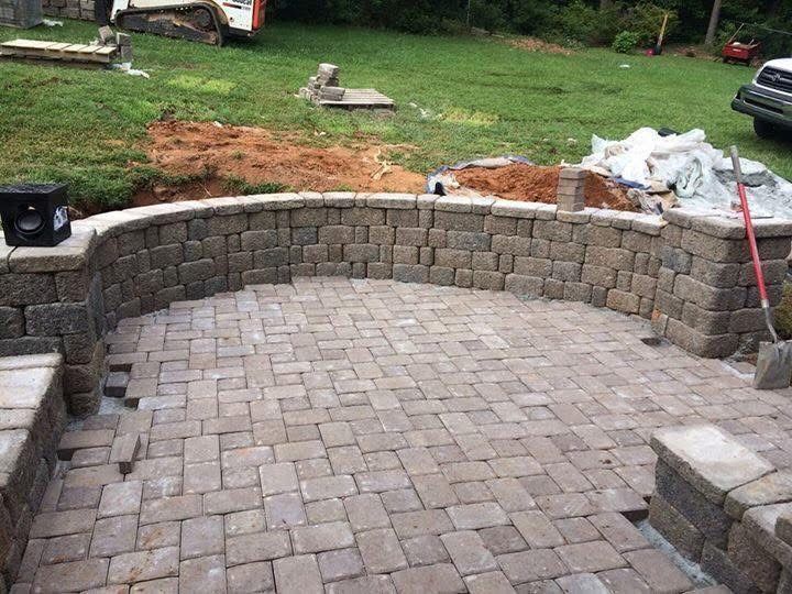 Patio construction: brick pavers and retaining wall. Construction equipment and materials in the background.