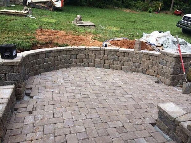 Patio construction: brick pavers and retaining wall. Construction equipment and materials in the background.