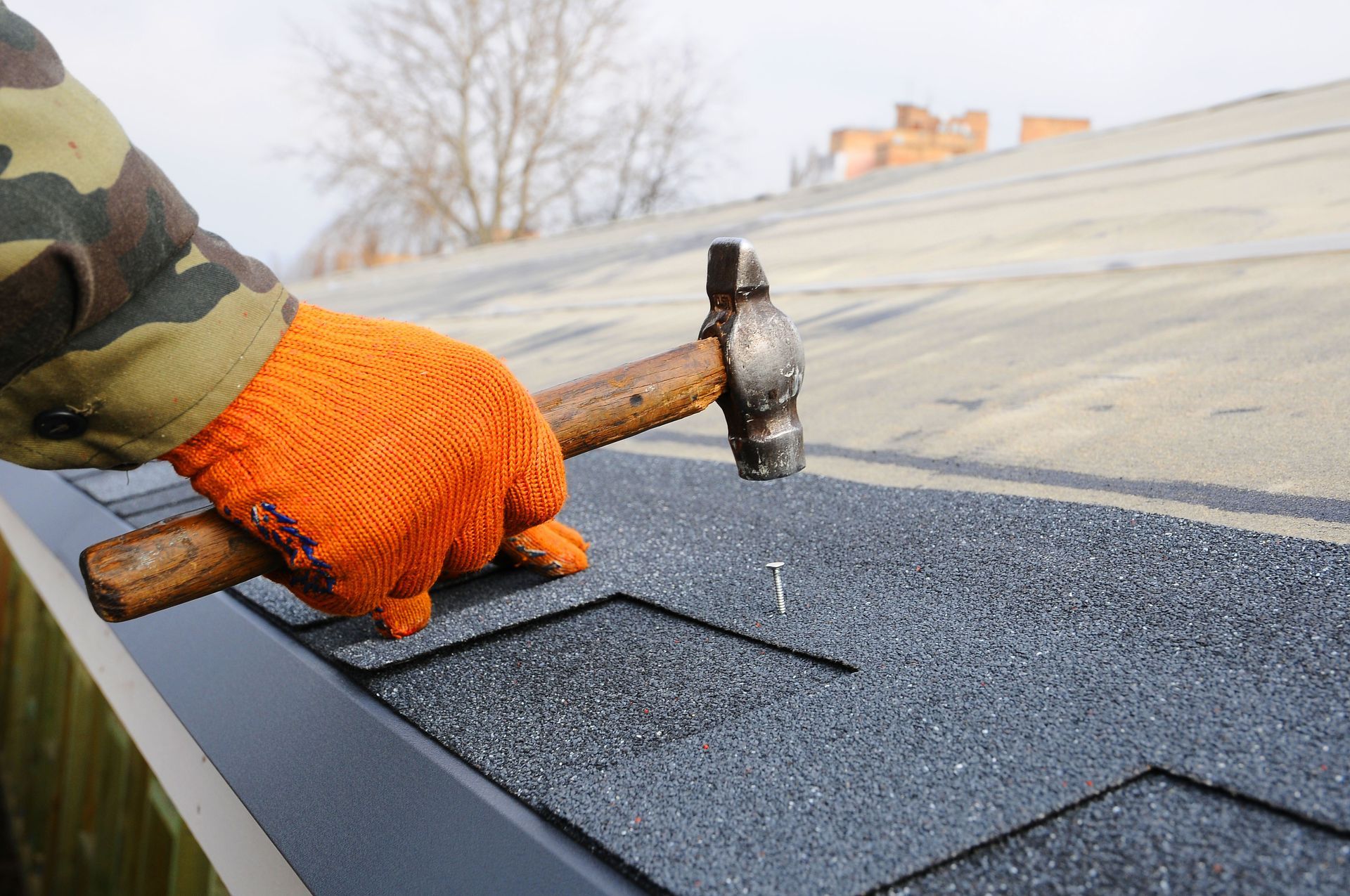 Gloved hand hammering roofing shingles on a roof edge