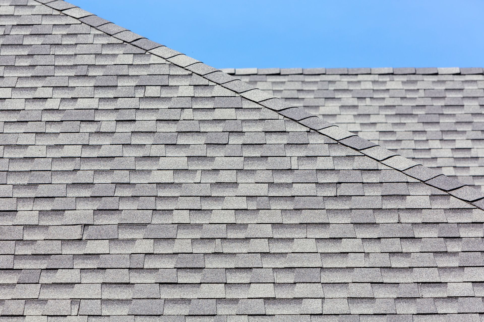 Gray shingled roof with a diagonal ridge against a blue sky