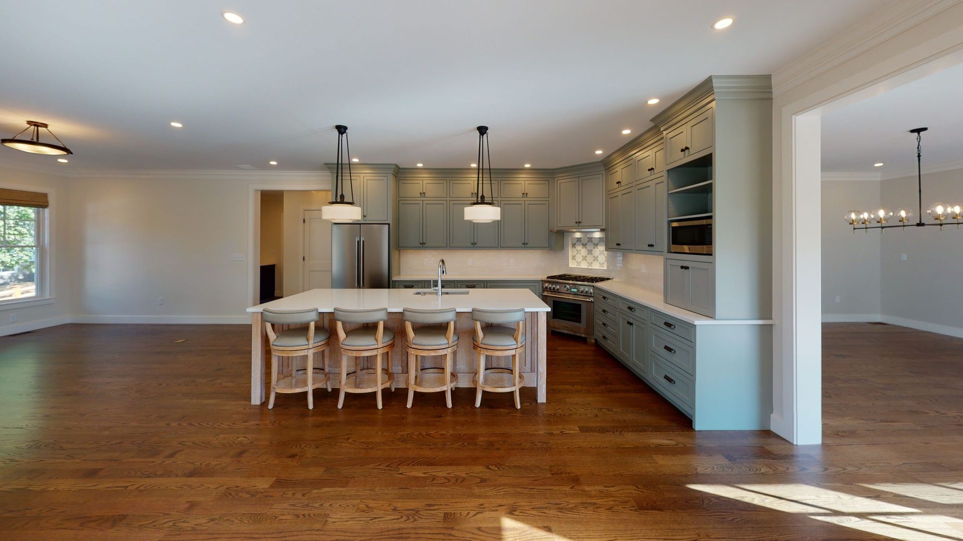 Open-concept kitchen with island and bar stools, hardwood floors, and gray cabinets.