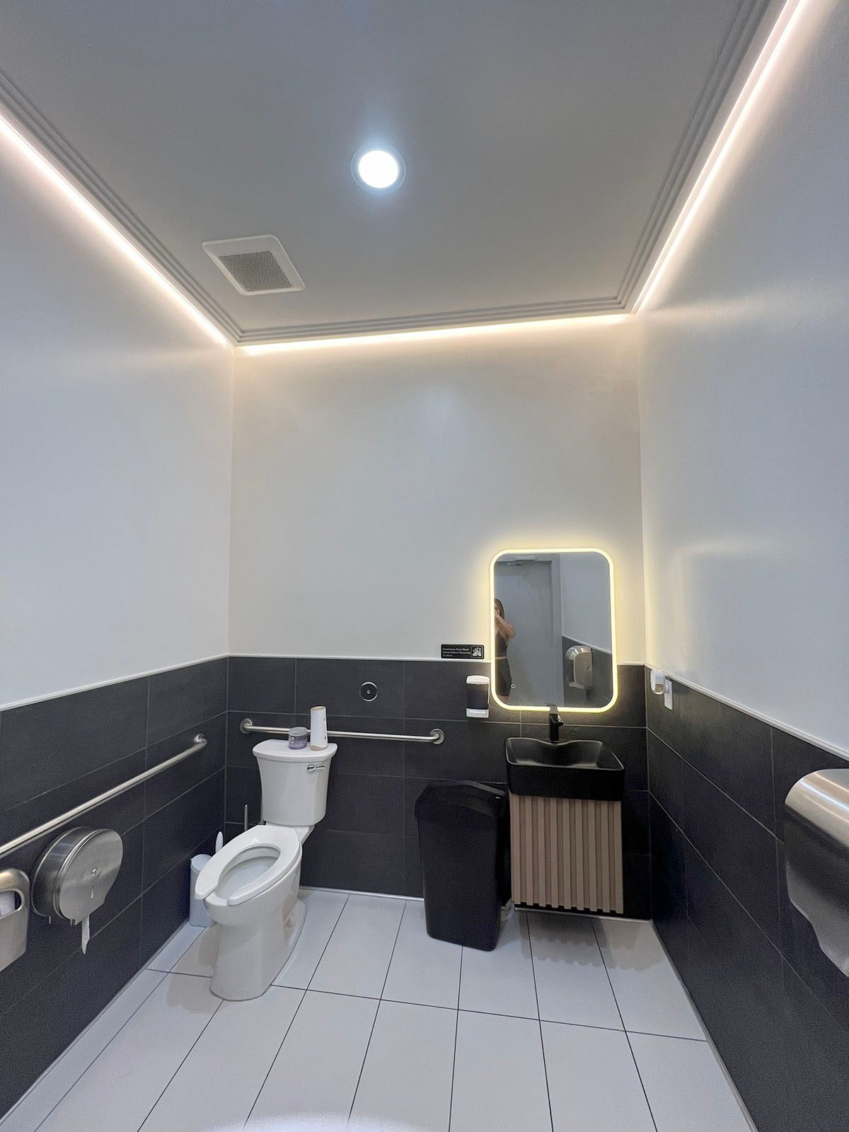 A well-lighted restroom with white walls and dark tile