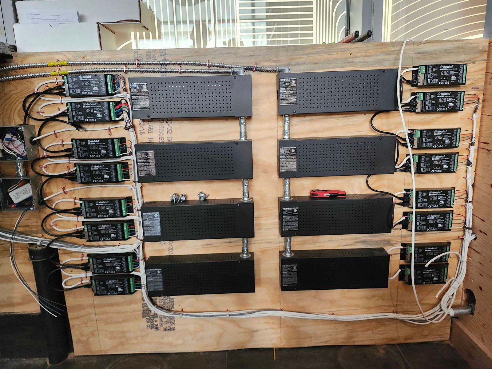 A wooden panel with rows of black power supplies and smaller black boxes wired together