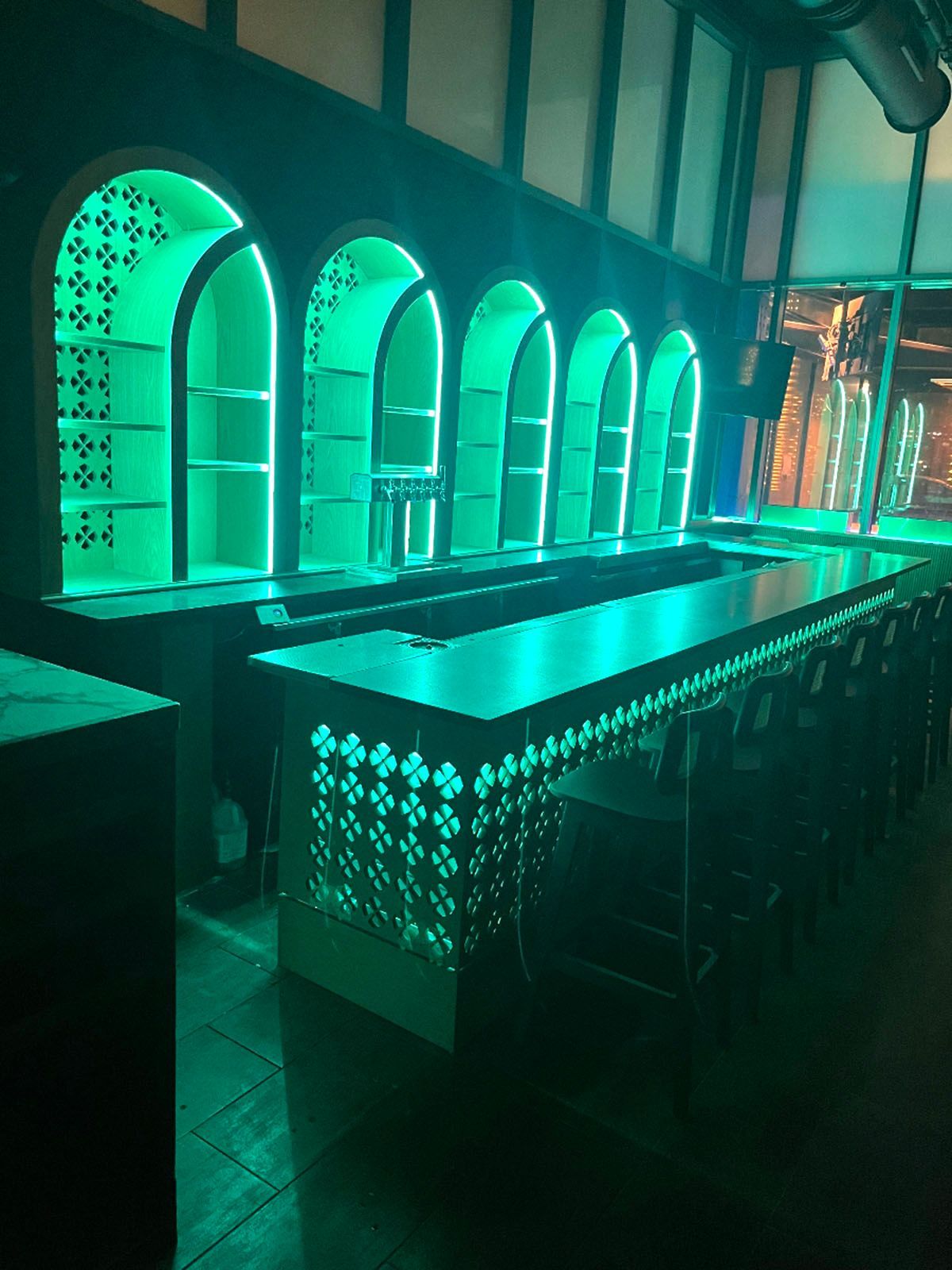 Green-lit bar with arch shelving and a long counter