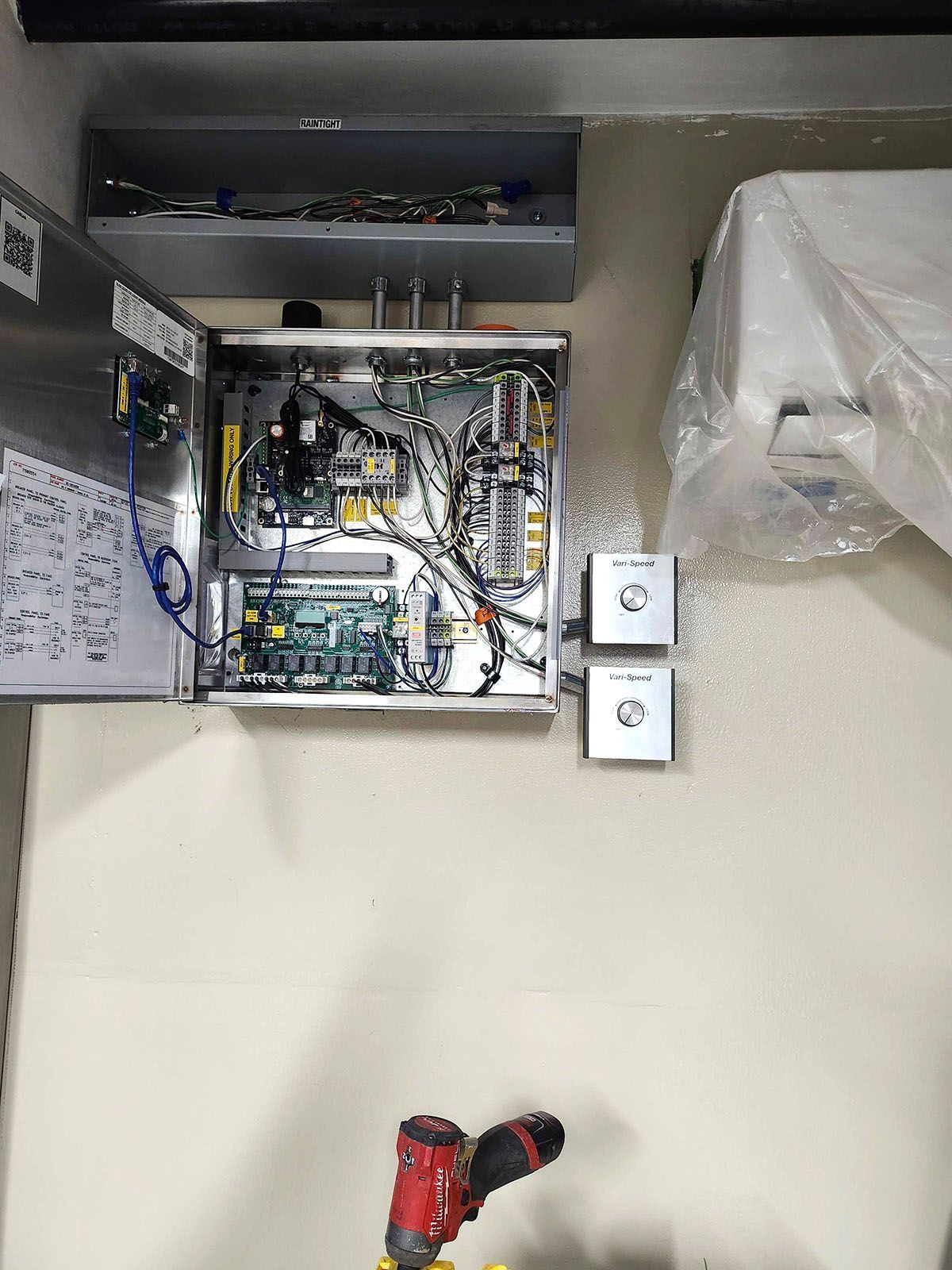 Open electrical panel with circuit boards and wiring on a beige wall