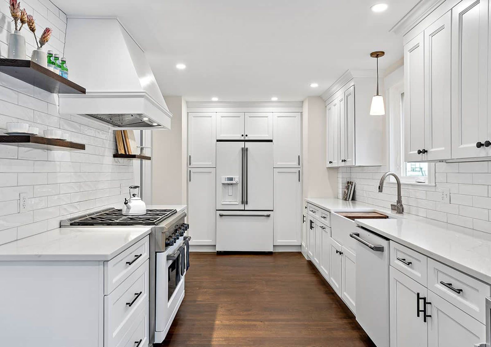 Well-lighted white modern kitchen with white cabinets, stainless steel appliances, and dark hardwood floors