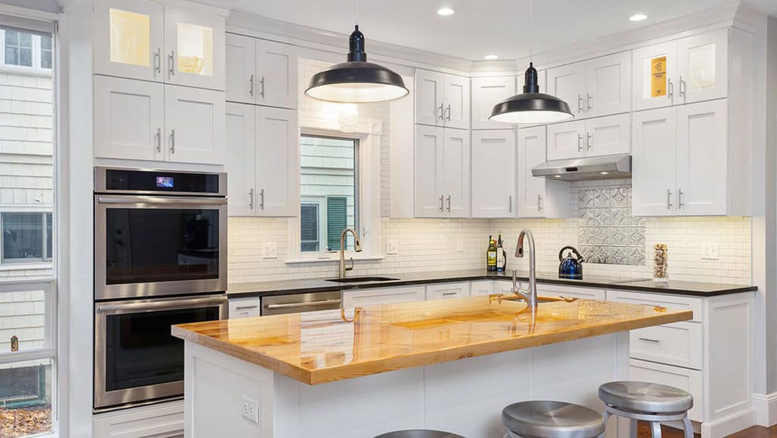 White kitchen with stainless steel appliances, butcher block island, and black pendant lights