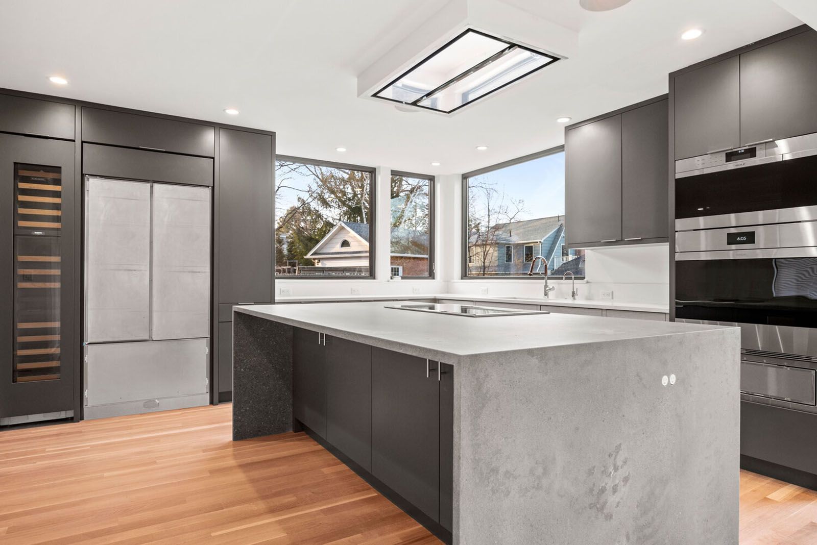Well-lighted modern gray kitchen with island, stainless steel appliances, and large windows