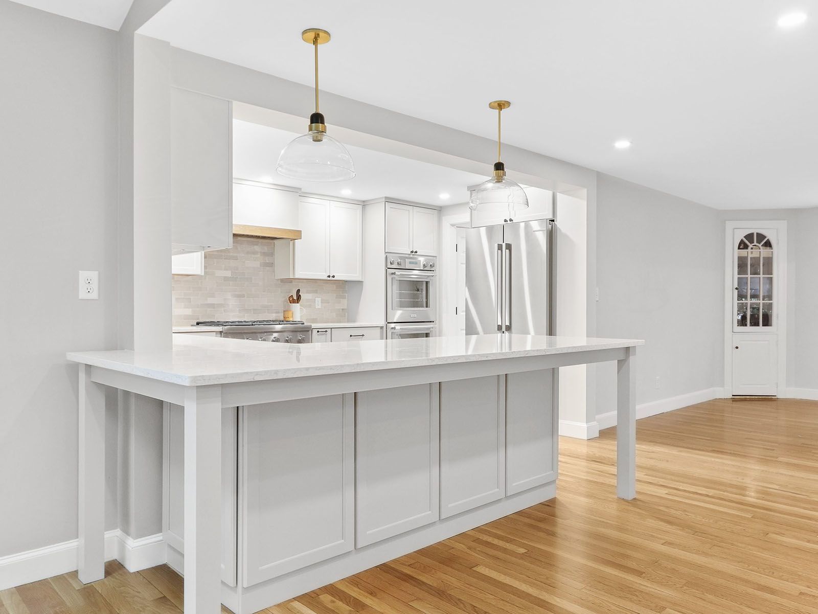 White kitchen with a breakfast bar, hardwood floors, and gold pendant lights