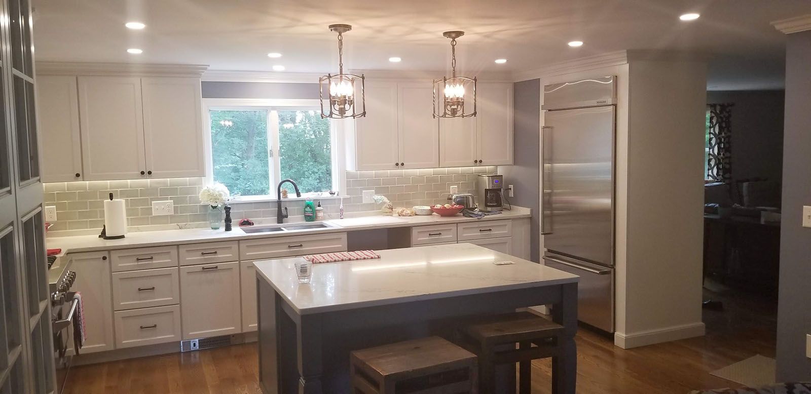 Well-lighted modern kitchen with white cabinets, island, and stainless steel refrigerator