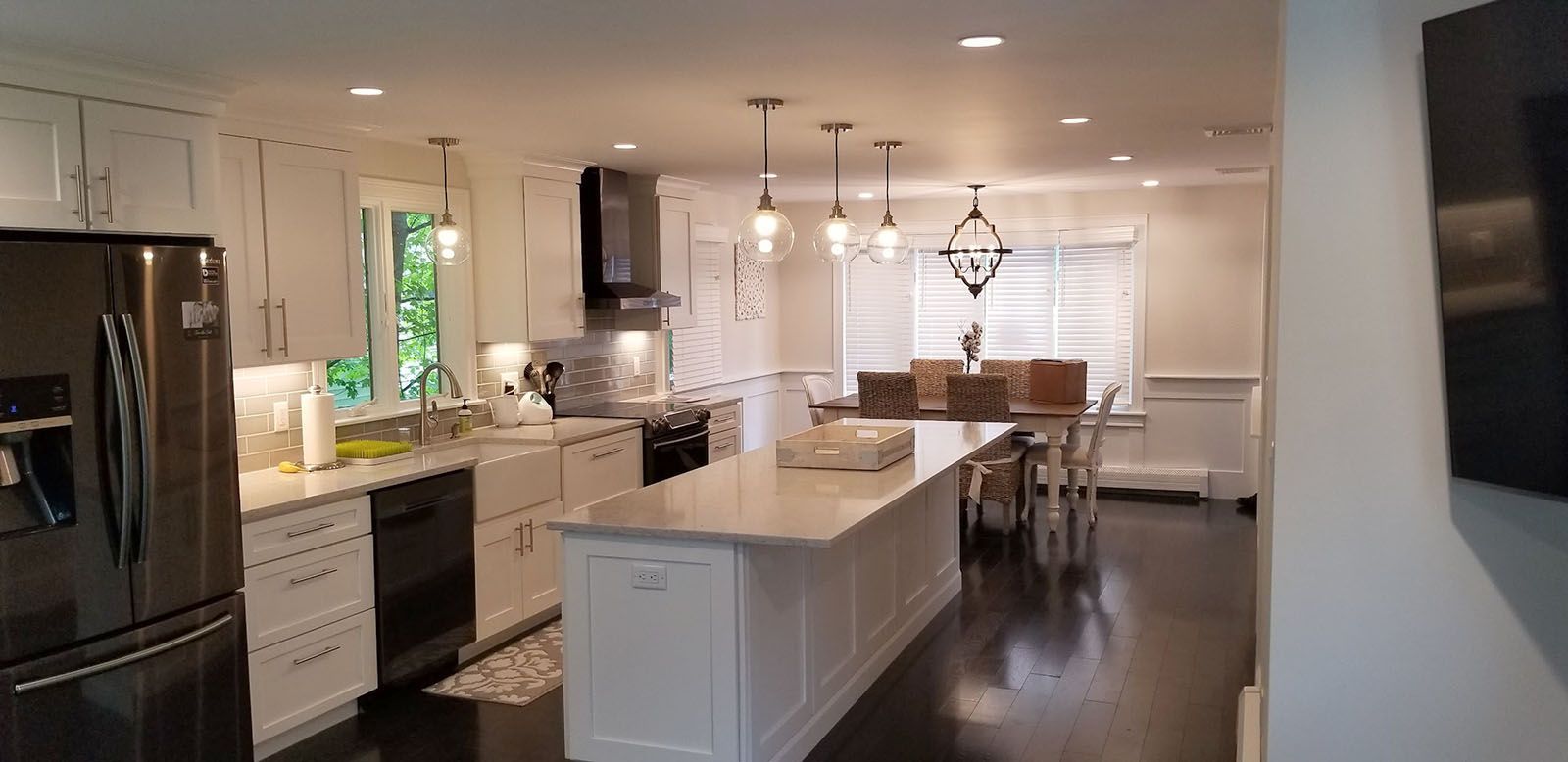 Spacious white kitchen with island, dark wood floors, and dining area with pendant lights.