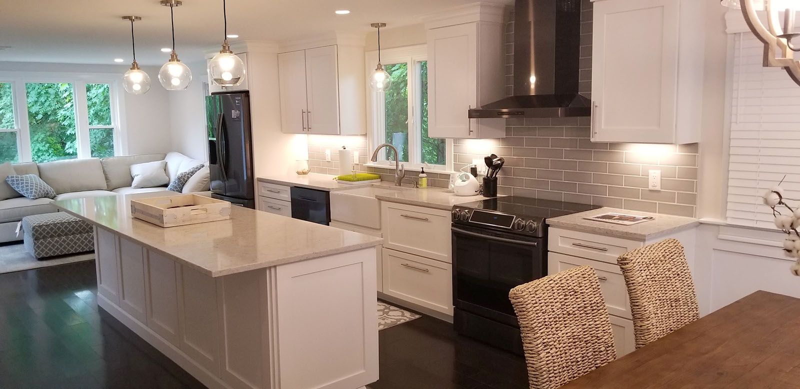 A well-lighted modern white kitchen with an island, dark floors, and stainless steel appliances