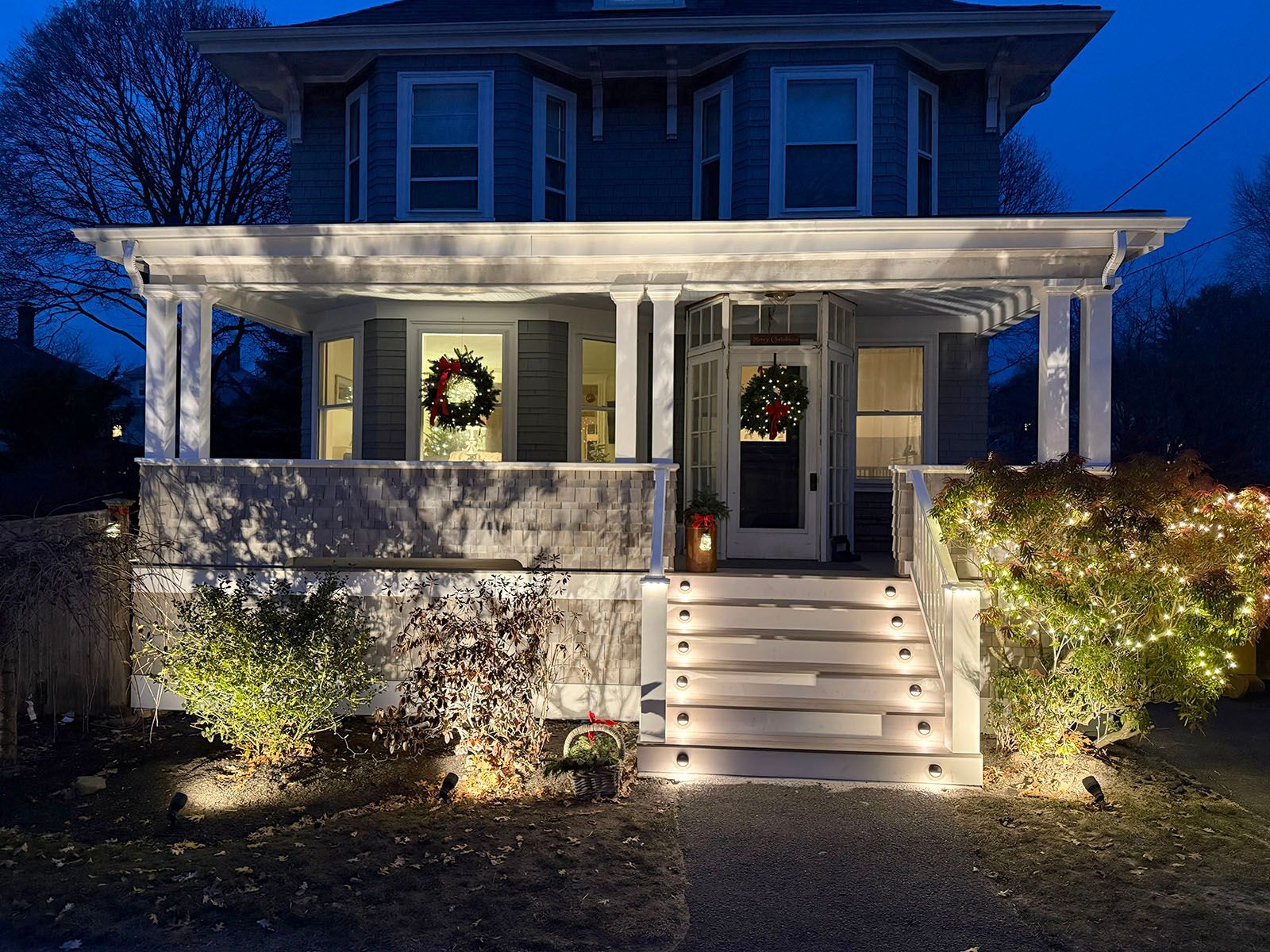 Lit-up blue house with Christmas decorations; wreath on the door, and lights on steps