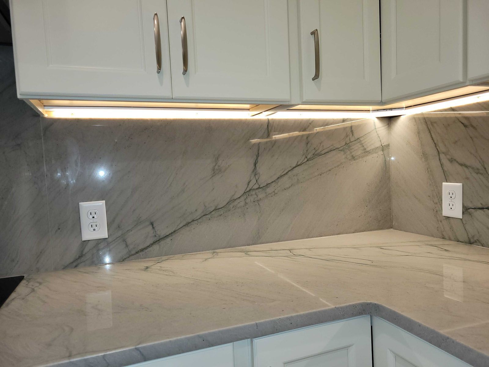 White kitchen cabinets with marble backsplash and countertop, under cabinet lighting.